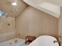 Modern luxury bathroom with freestanding white soaking tub, walk-in shower, wood-paneled walls, and skylights