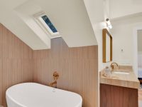 Modern bathroom with white freestanding oval bathtub, wooden vanity, mirror, and skylight in ceiling