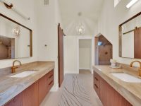 Spacious primary bathroom with dual vanities, marble countertops, wood cabinetry, and large mirrors with sconces