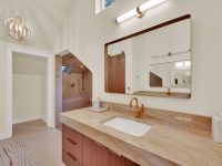 Modern bathroom with dual vanity, wooden countertop, large mirror, and white walls with recessed lighting