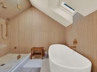Modern luxury bathroom with wooden walls, freestanding oval bathtub, walk-in shower, and warm lighting fixtures