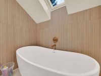 Modern bathroom with white oval freestanding bathtub, wood-paneled walls, skylight, and minimalist décor