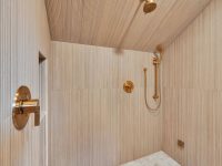 Modern wooden shower enclosure with brass fixtures, white tile floor, and vertical wood paneling throughout