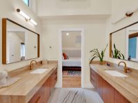 Spacious master bathroom with dual vanities, large mirrors, wooden countertops, and view into bedroom through open doorway