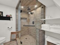 Modern bathroom with glass-enclosed walk-in shower, white subway tile walls, floating shelves with towels, and wood-look flooring