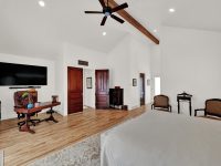 Spacious bedroom with vaulted ceilings, wooden floors, wall-mounted TV, and modern furnishings including red accent pieces