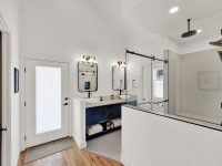 Modern bathroom with white vanity, double sinks, large mirror, glass shower enclosure, and wood flooring