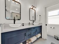 Modern bathroom with dual sinks, navy blue vanity, black-framed mirrors, white subway tile walls, and a door with frosted glass panel