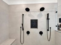 Modern walk-in shower with multiple black rainfall and body spray showerheads mounted on white tile walls