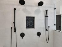 Modern bathroom shower with multiple black showerheads and fixtures mounted on gray tile walls