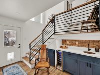 Modern kitchen with dark blue cabinetry, white subway tile backsplash, and metal staircase with wood railing leading to loft space