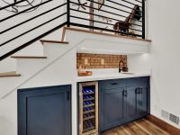 Modern kitchen with dark blue cabinetry, wine cooler, and wooden stairs with metal railings overhead