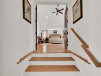 Wooden staircase with white walls leading to a bedroom with a ceiling fan and framed artwork on the side walls