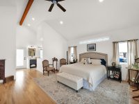 Spacious master bedroom with vaulted ceiling, wooden beams, hardwood floors, and elegant furnishings including a bed and seating area