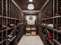 Wine cellar with wooden racks lining both sides, barrel at end, pendant lights overhead, and bottles stored on shelves