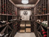 Elegant wine cellar with wooden racks lining both sides, stone flooring, decorative wreath, and ornate clock on far wall