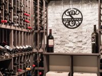 Wine cellar storage with wooden racks holding wine bottles and an ornate circular metal wall clock above cushioned seating