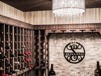 Elegant wine cellar showroom with dark wood wine racks, decorative circular metal wall art, marble accent wall, and crystal chandelier