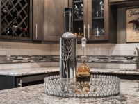 Elegant kitchen countertop with decorative bottle, crystal tray, and amber liquid, featuring dark cabinetry and granite counters in