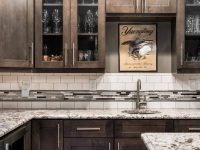 Modern kitchen with dark cabinetry, marble countertops, glass-front upper cabinets, and decorative backsplash tile