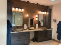 Modern bathroom vanity with dual sinks, dark cabinetry, large mirrors, and illuminated sconces above the countertop